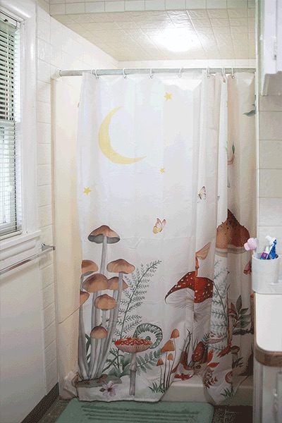 A white, tiled shower with mushroom-print shower curtain.